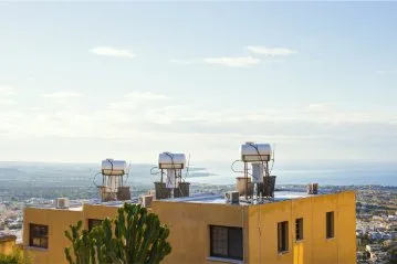 Ein Gebäude mit mehreren Solar-Wasser-Anlagen auf dem Dach, im Hintergrund eine weite Landschaft und das Meer.