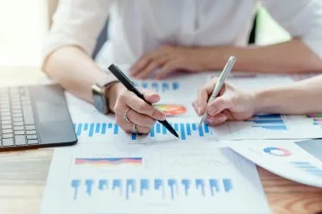 Zwei Personen arbeiten an einem Tisch mit verschiedenen Diagrammen und Grafiken.